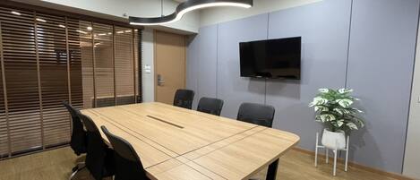 A conference room with a long table, black chairs, a flat-screen TV on the wall, and a potted plant.