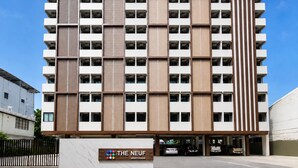 Een meerlaags gebouw met een modern ontwerp, met een combinatie van witte en bruine panelen, en een bord met de tekst 'THE NEUF' en een logo.