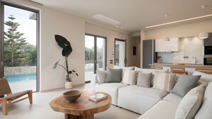 Una sala de estar moderna con un amplio sofá modular, una mesa de centro de madera y vista a una piscina.