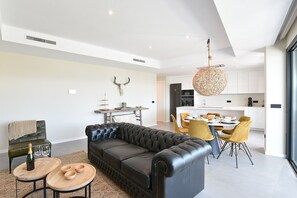 Un salon moderne avec un canapé en cuir, un coin repas avec des chaises jaunes et une cuisine dotée de meubles blancs.