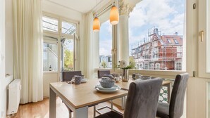 Een eethoek met een tafel gedekt voor twee personen, een uitzicht op een stadsbeeld met gebouwen in aanbouw, en een groot raam met gordijnen.