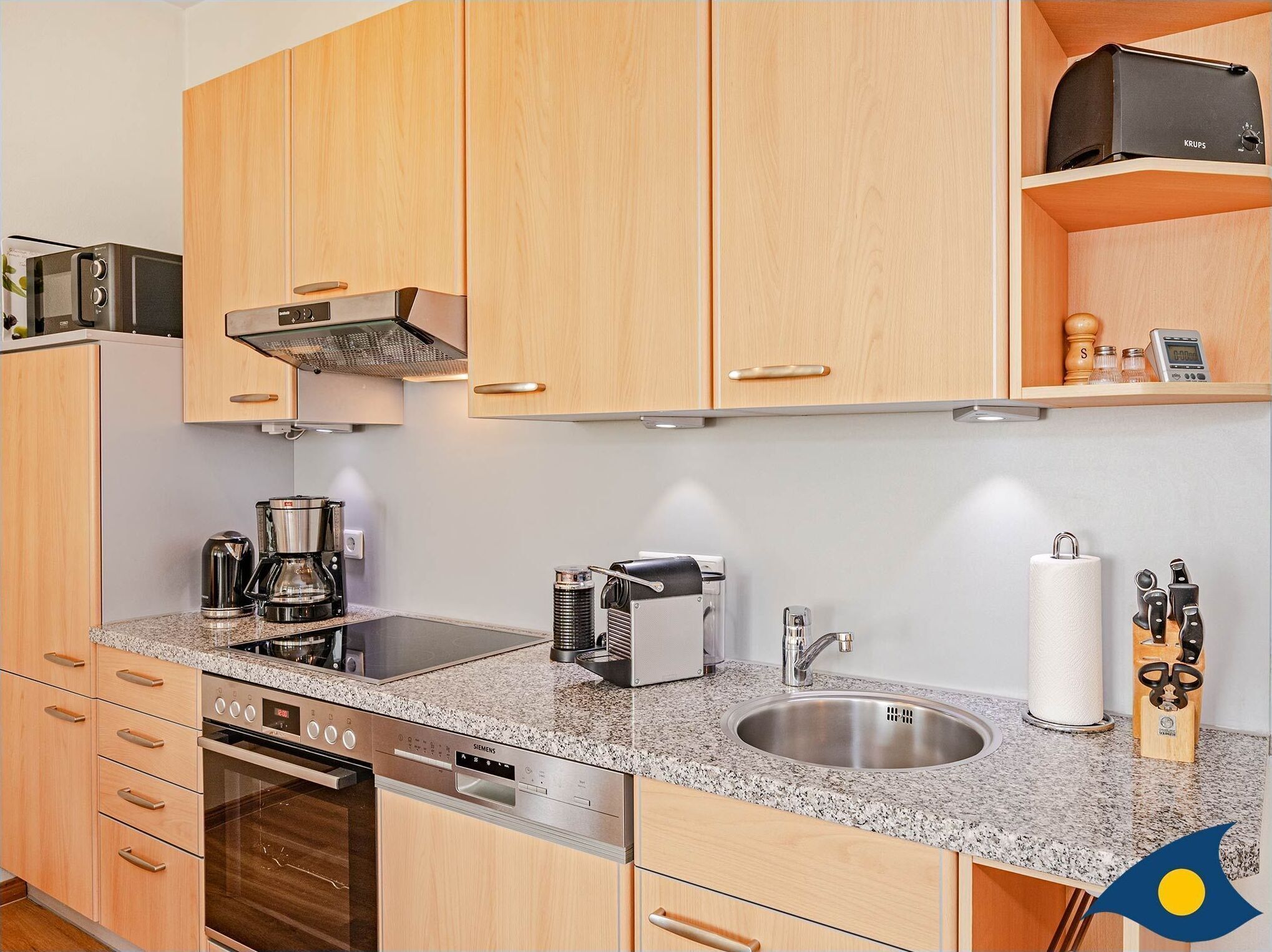 Una cocina moderna con armarios de madera, un lavamanos de acero inoxidable, una cafetera y un lavavajillas Siemens.