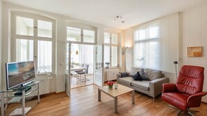 Een ruime woonkamer met een houten vloer, een grijze bank, een rode lederen fauteuil en een glazen salontafel.