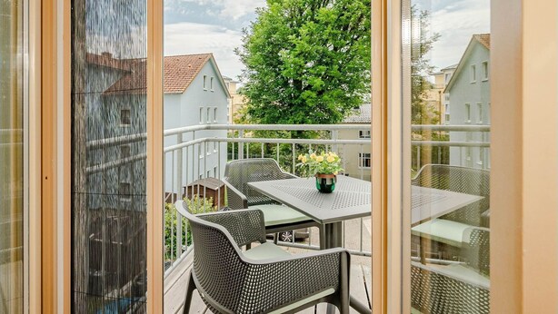 Een balkon met een tafel en stoelen, een bloempot en uitzicht op huizen en bomen.
