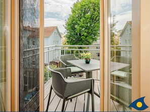 Un balcon avec une table et des chaises, un pot de fleurs et une vue sur des maisons et des arbres.