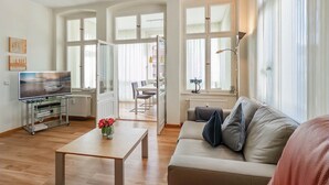 Een ruime woonkamer met een bank, een salontafel en een televisie op een glazen voet.