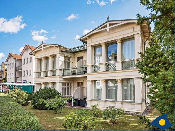 Un immeuble à plusieurs étages doté de balcons, de grandes fenêtres et d’un jardin bien entretenu.