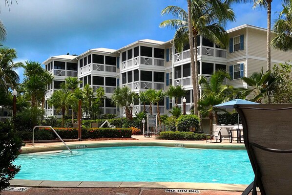A hotel with a pool, surrounded by palm trees and a clear sky.