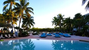 Zona de piscina con sillones de descanso y palmeras.