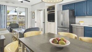 Una cocina moderna con armarios azules, un refrigerador de acero inoxidable y un comedor con sillas de mimbre y un cuenco de fruta.