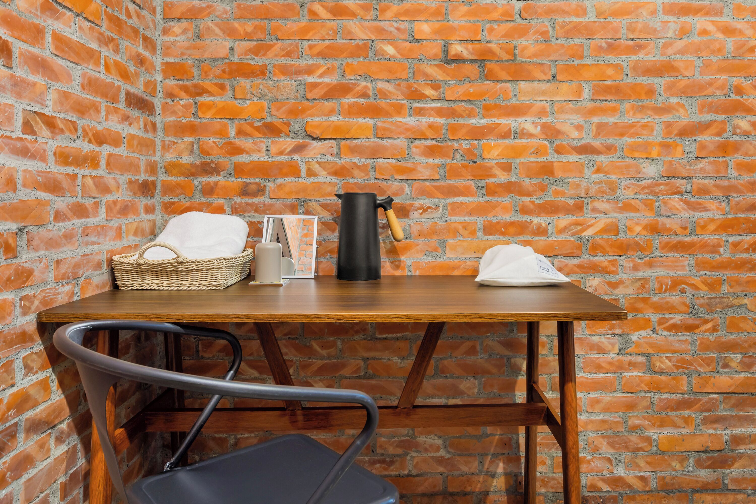 Une petite pièce accueillante avec un mur en briques, une table en bois, une chaise, un panier, une bouilloire et une serviette blanche.