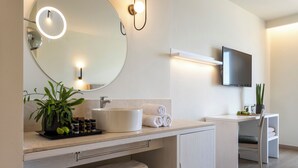 Un baño moderno con un espejo redondo, un lavabo, un televisor montado en la pared y una silla.