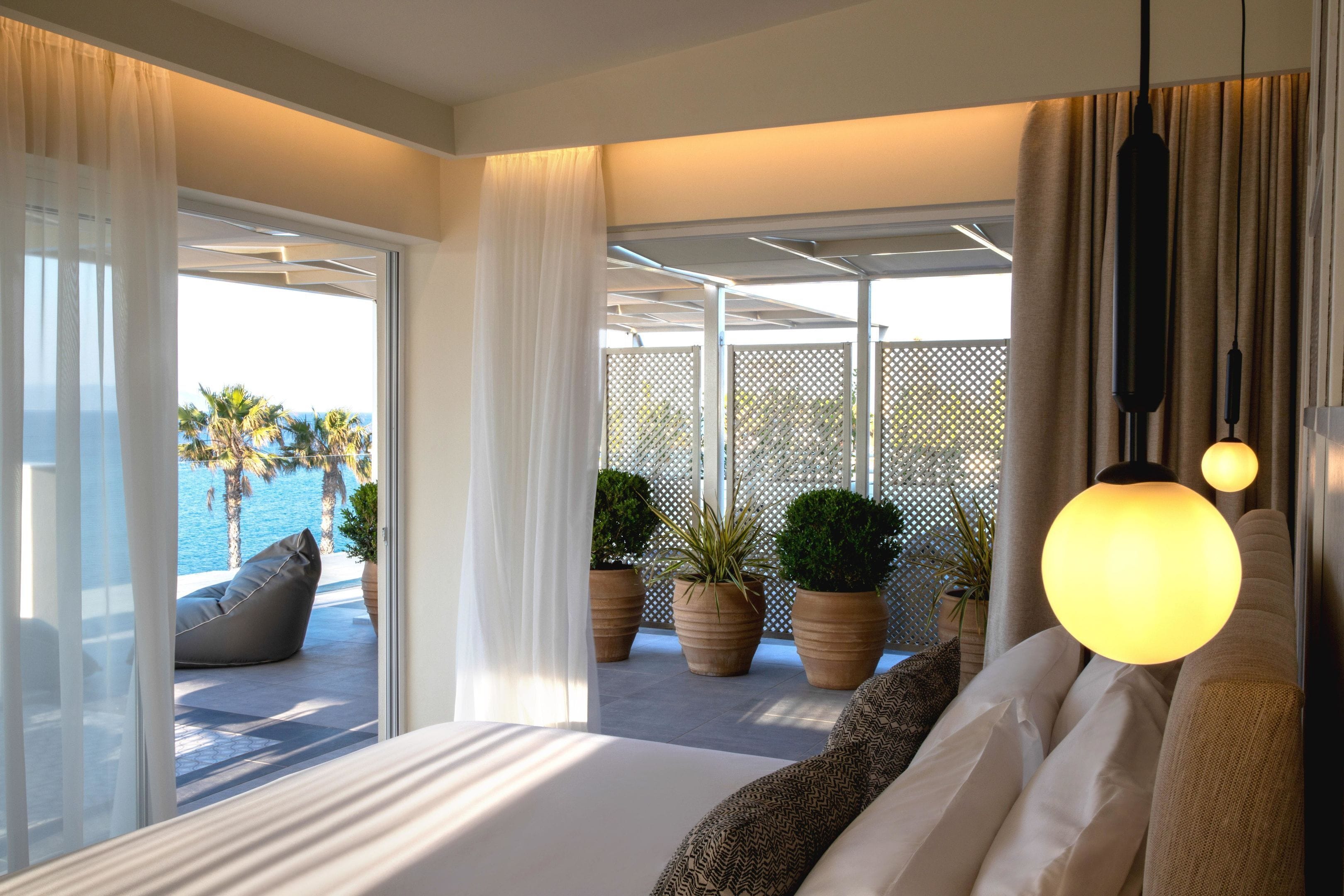 A bedroom with a large bed, a view of the pool, and potted plants.