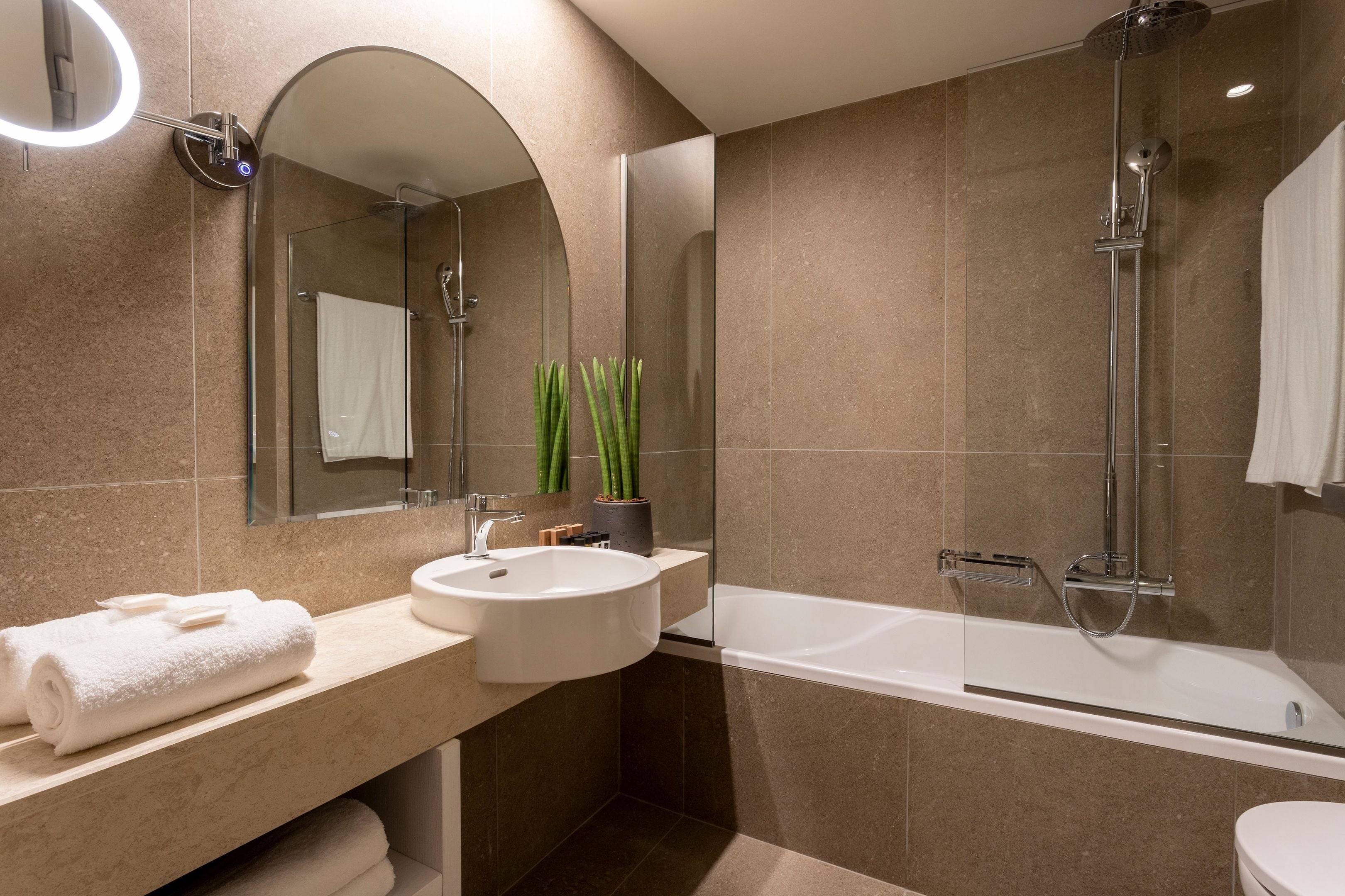 A modern bathroom with a large mirror, a sink, a bathtub, and a shower.