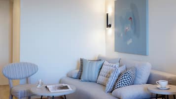 Una sala de estar moderna con un sofá gris, un sillón a rayas y una pequeña mesa redonda con un vaso de agua y una taza.