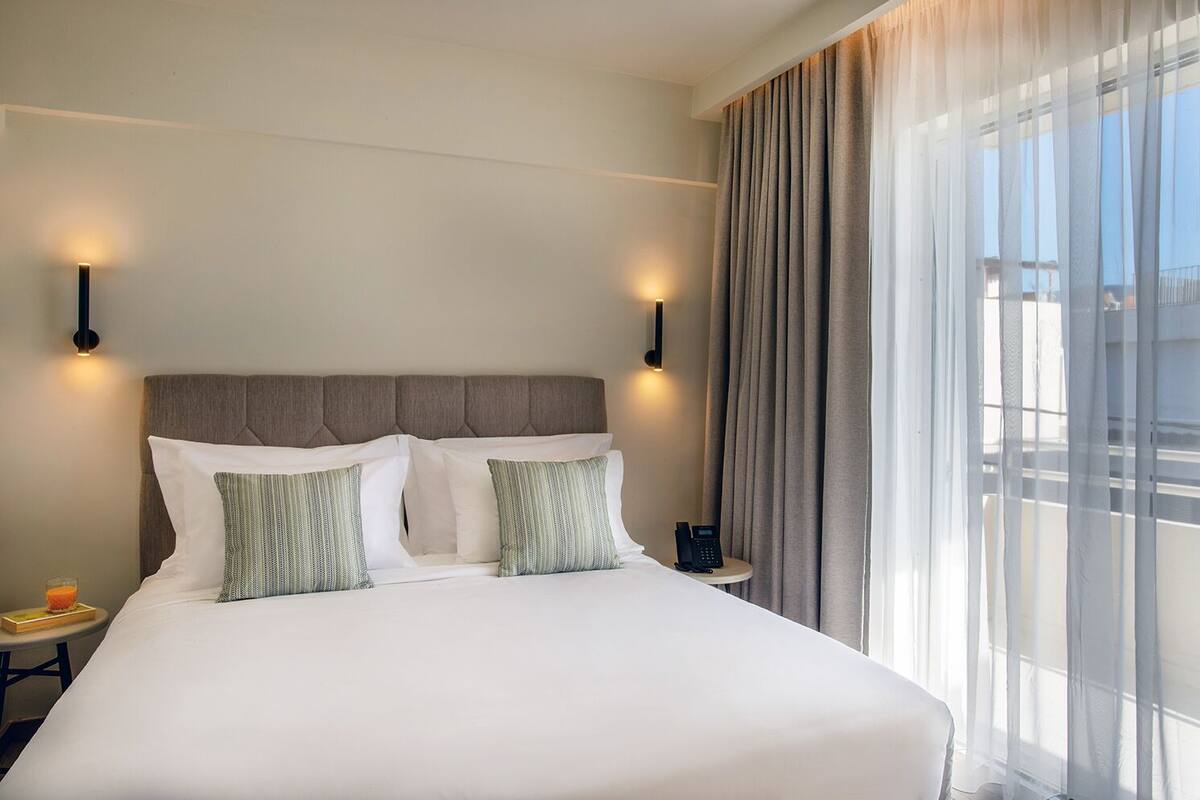 Een hotelkamer met een groot bed, twee nachtkastjes, een telefoon op het nachtkastje en een raam met gordijnen.