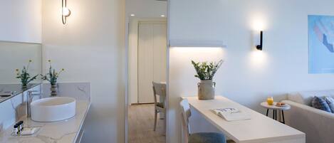 A modern, well-lit room with a marble sink, a dining area with a vase of flowers, a sofa, and a small table with a book.