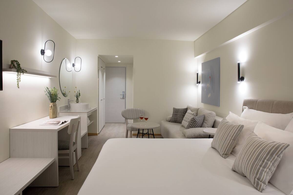 Een moderne hotelkamer met een groot bed, een bureau, een klein rond tafeltje en een sofa.