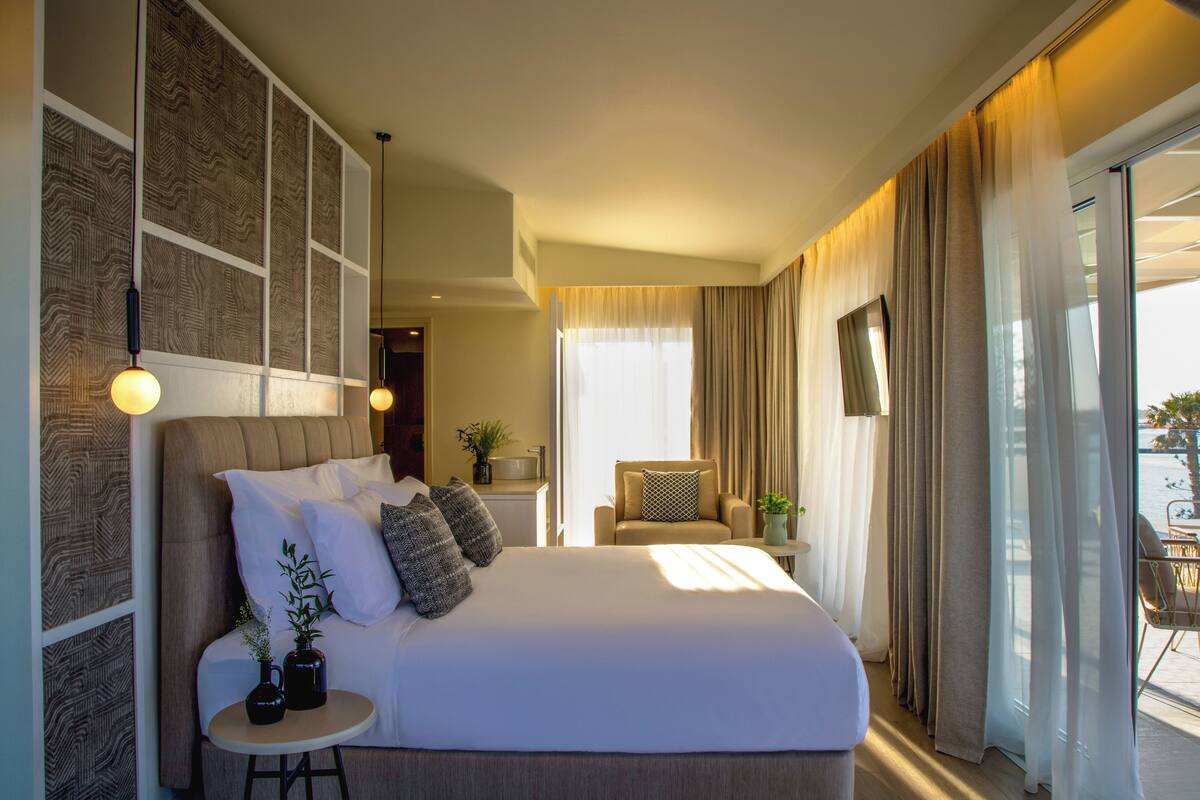 Hotelkamer met een groot bed, een tafeltje met twee planten in potten, een stoel en uitzicht buiten via een schuifdeur.