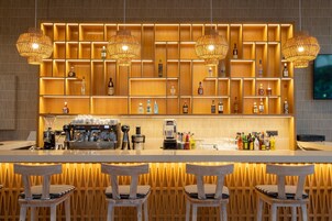 Zona de bar con una estantería de madera que exhibe varias botellas, una máquina de café y taburetes de bar.