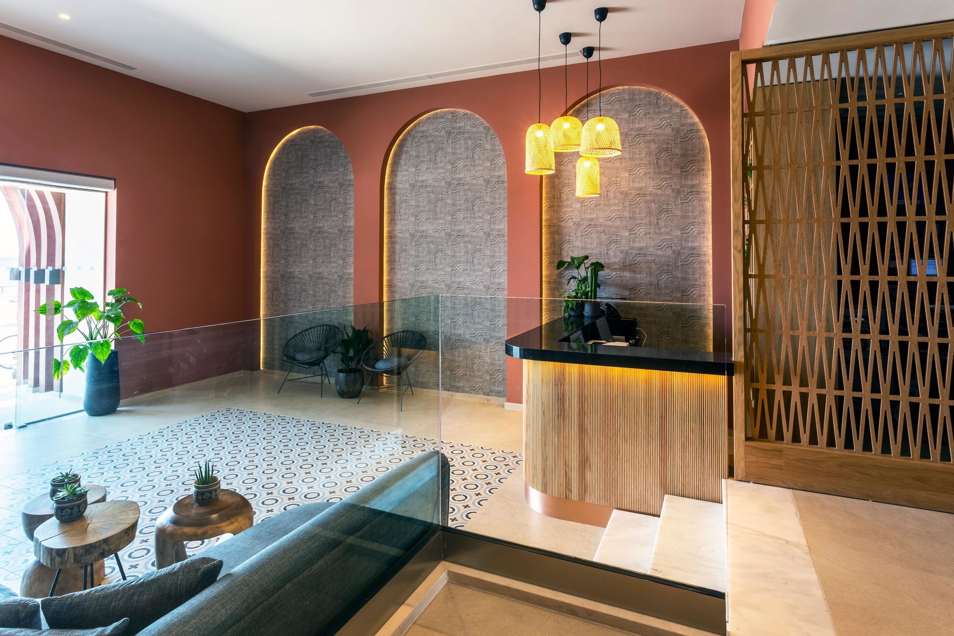 A modern lobby with a glass partition, a reception desk, and a seating area with a sofa and small tables.
