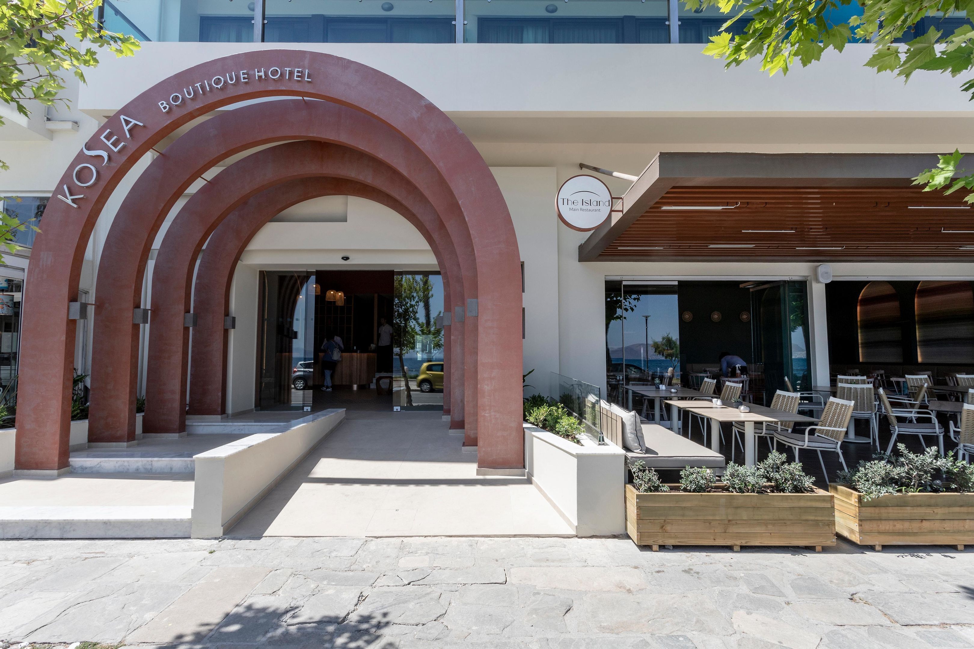 La entrada del Hotel Boutique Kosea, con un diseño moderno, zona de estar al aire libre y un restaurante visible llamado "The Island".