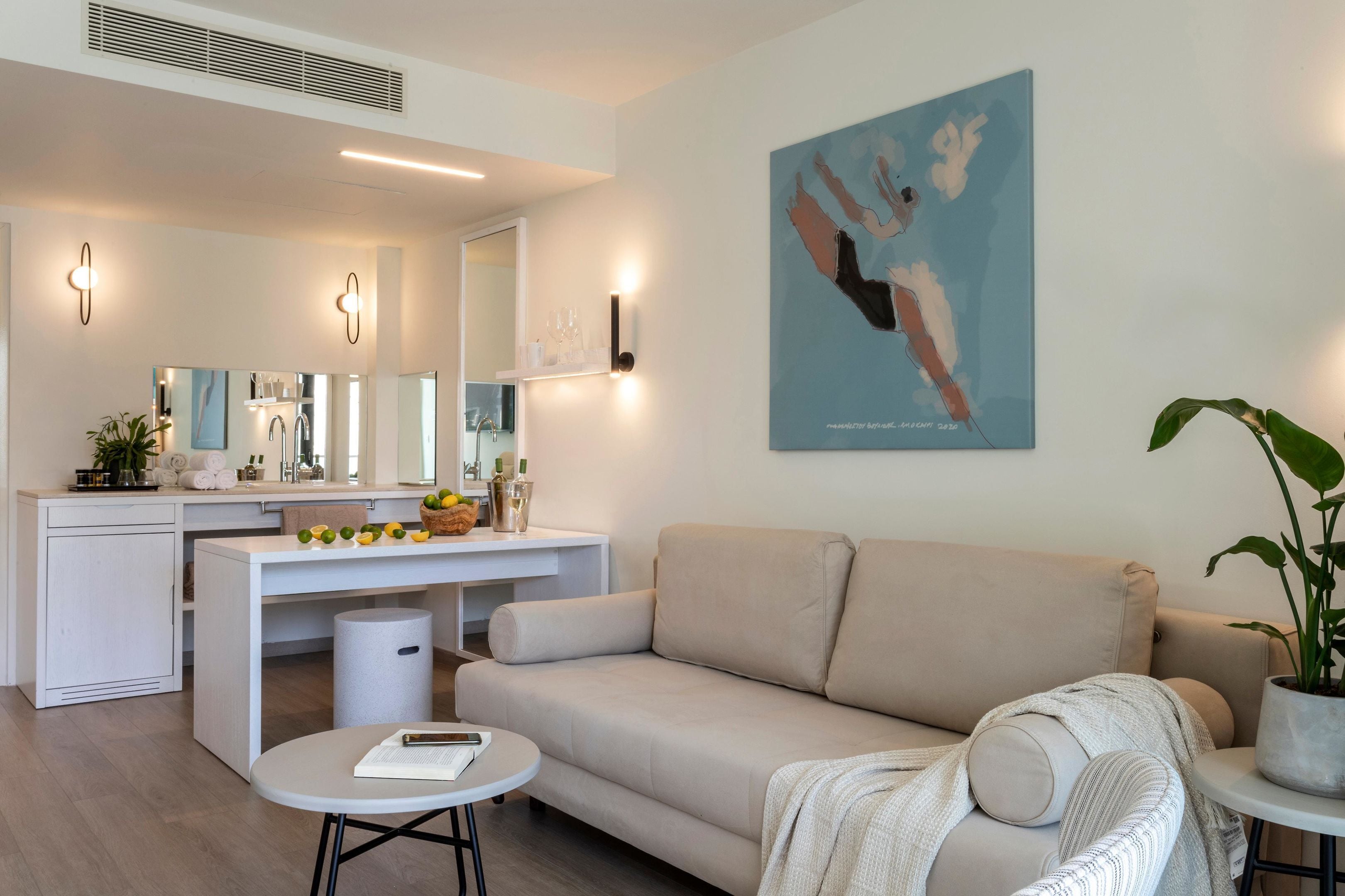 Un salon moderne comprenant un canapé, une petite table ronde, un meuble blanc et un coin cuisine avec un plan de travail et un évier.