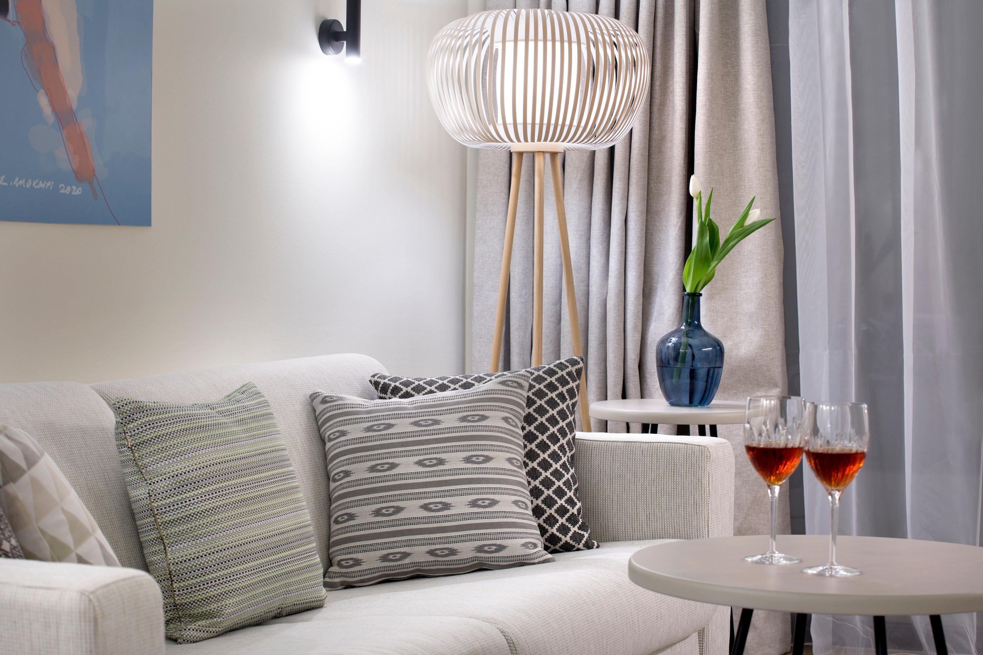 En moderne stue med en sofa, mønstrede puder, et rundt bord med to glas rødvin, en blå vase med en plante og en hængende lampe.
