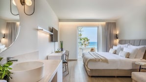 Habitación de hotel moderna con una cama grande, un lavamanos blanco redondo, un escritorio y un balcón con vistas al mar.