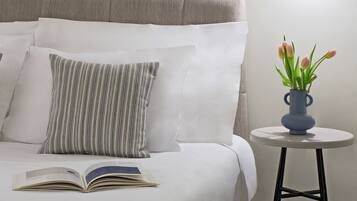 A neatly made bed with white linens and striped pillows, an open book on the bed, and a small table with a vase of tulips.