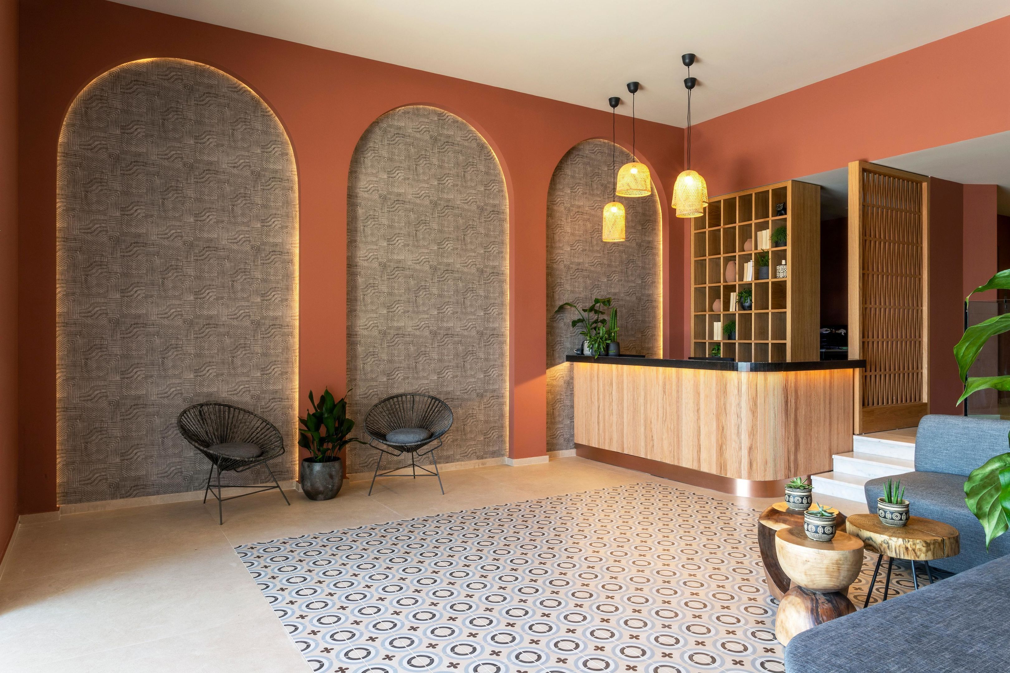 Un área de recepción con mostrador de madera, dos sillas, una alfombra estampada y una escalera que sube a otro nivel.