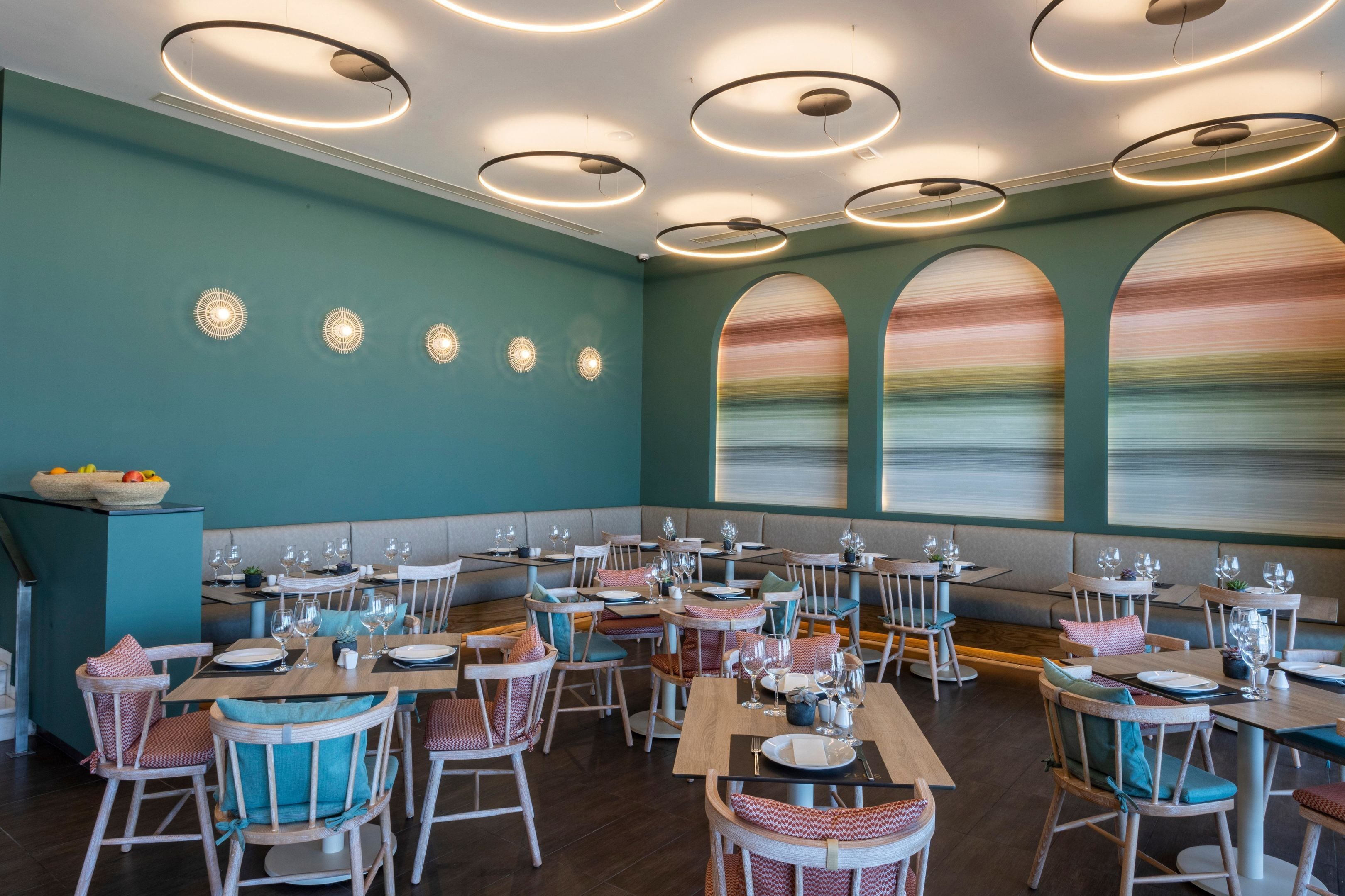Un restaurante con mesas redondas, sillas y una pared color esmeralda.