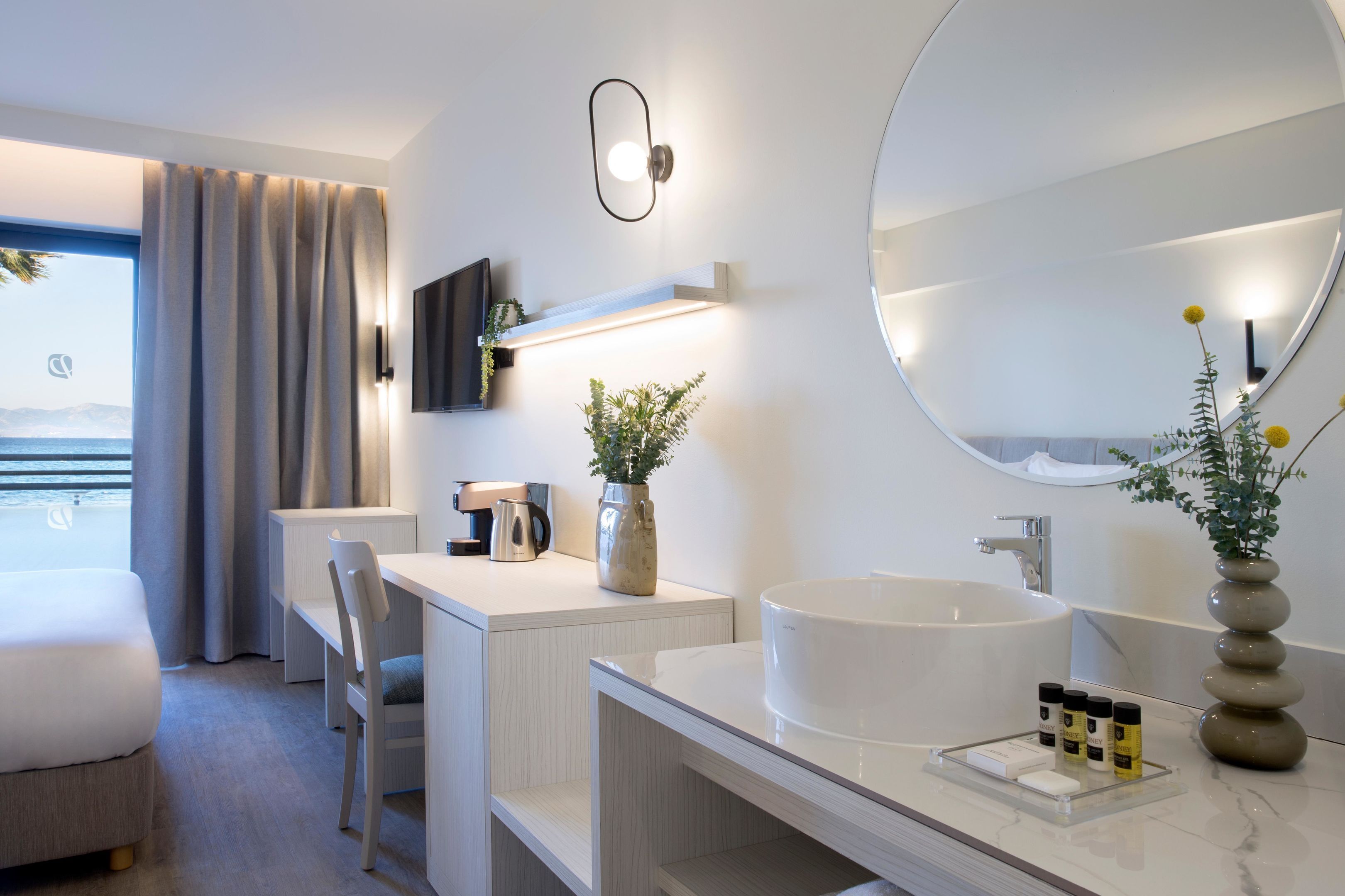 Habitación de hotel moderna con una cama grande, un escritorio, un baño con espejo amplio y vista al mar.