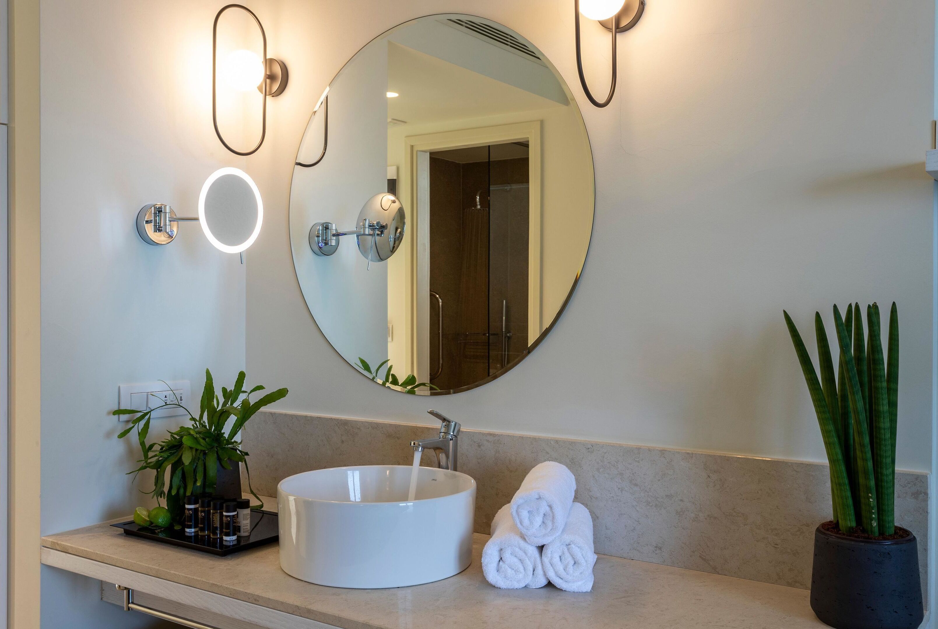 A bathroom with a round mirror, a sink, and a potted plant.
