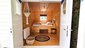 A cozy cabin-style room with a bed, a hanging light fixture, a small window, and a wooden floor. - Chalet Kieftveen with hot tub for four Person (Voorthuizen)