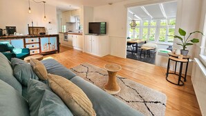 A spacious living room with a sofa, a coffee table, and a TV. There is a kitchen area with cabinets and a dining table. - Chalet Kieftveen with hot tub for four Person (Voorthuizen)