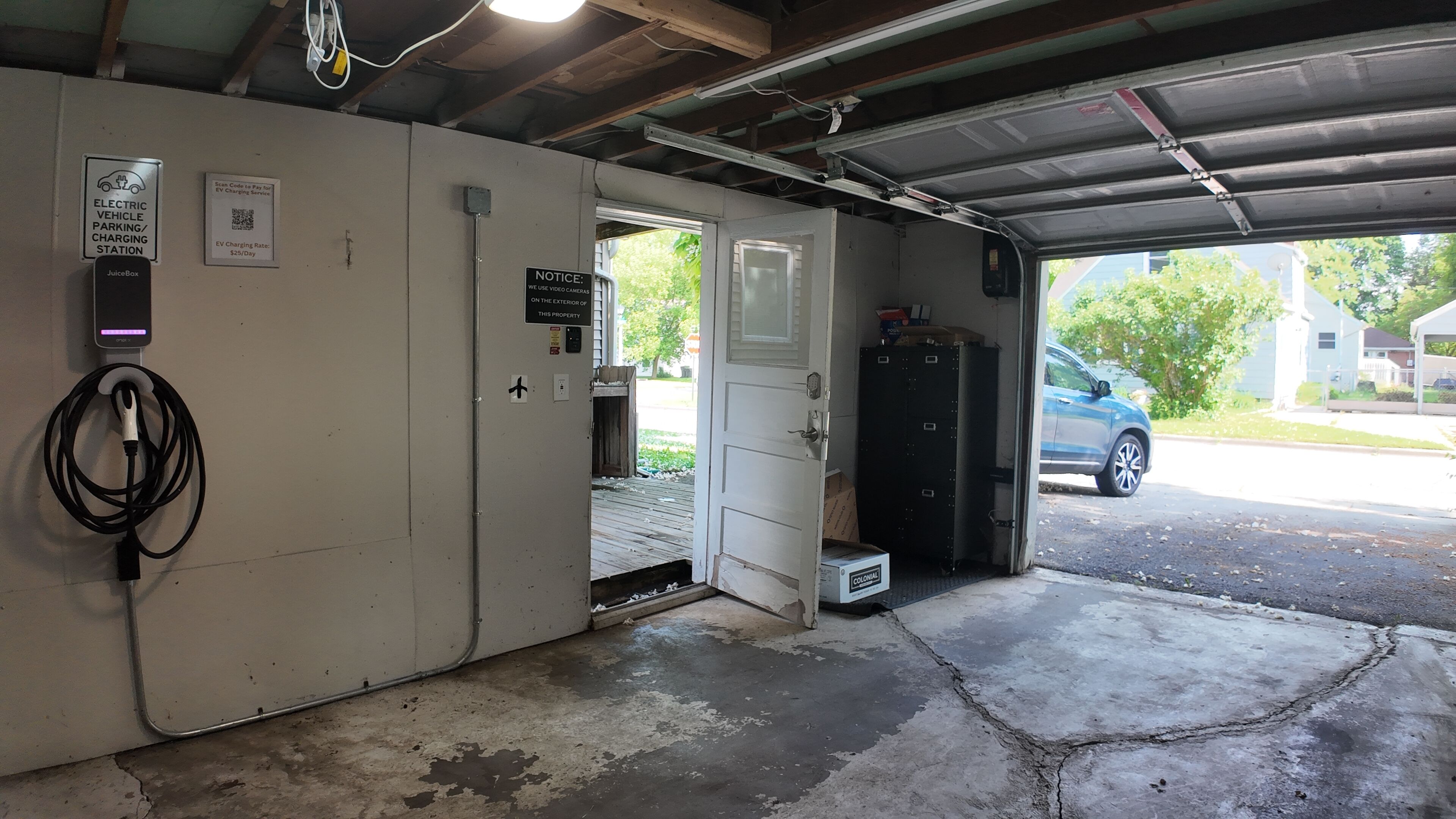 Een laadstation voor elektrische voertuigen met een JuiceBox oplader, een melding over beveiligingscamera's en een bord met het laadtarief.