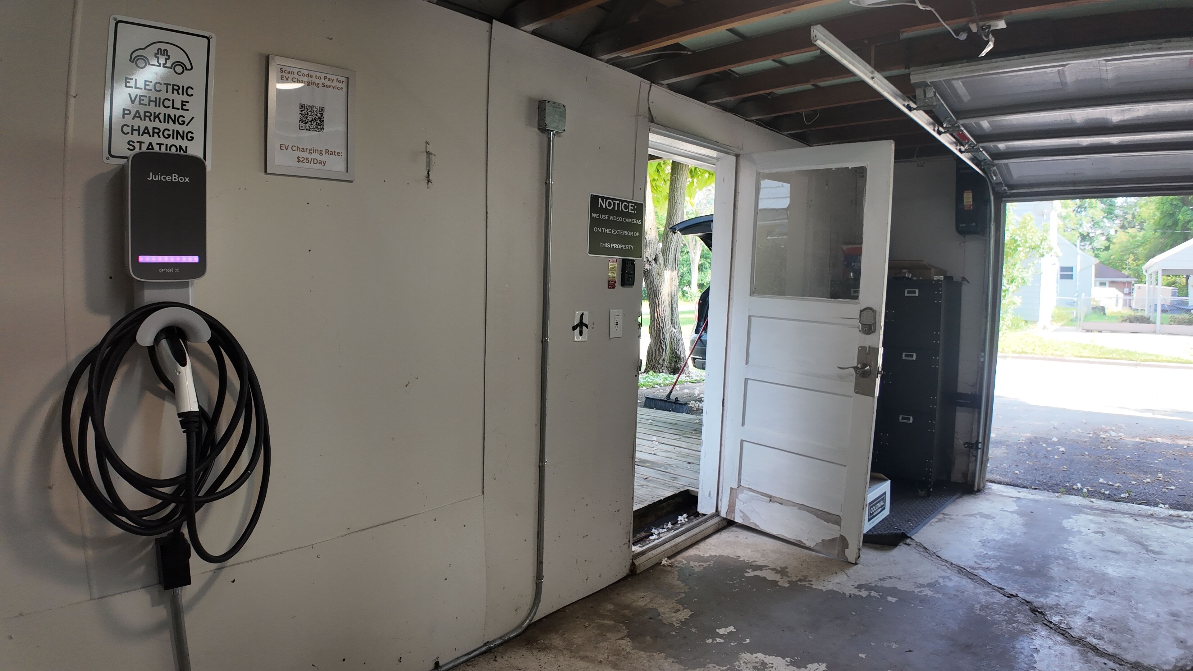 Una estación de carga para vehículos eléctricos con un cargador JuiceBox, un aviso sobre cámaras de video e información sobre la tarifa de carga para vehículos eléctricos.