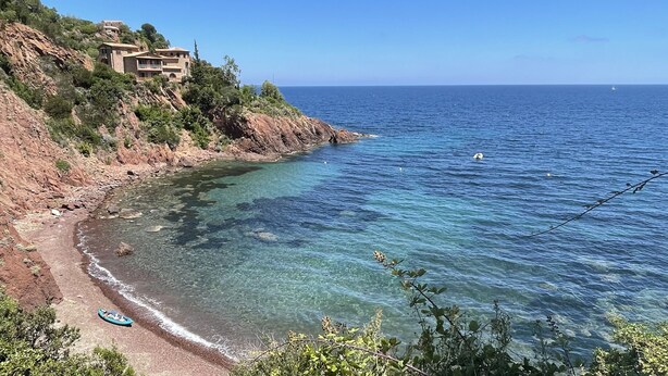 Una zona costera con aguas cristalinas, una playa de rocas y un edificio en la ladera de una colina.