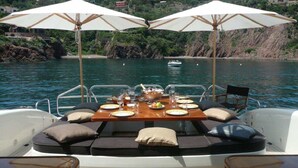 Un bote con una mesa lista para dos, rodeado de asientos acolchados y dos sombrillas.