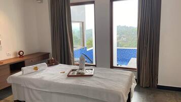 Relax in a spacious room with a large bed, two windows, and a nightstand with a clock and amenities.