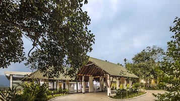 A building with a covered patio area, surrounded by greenery and a paved walkway.