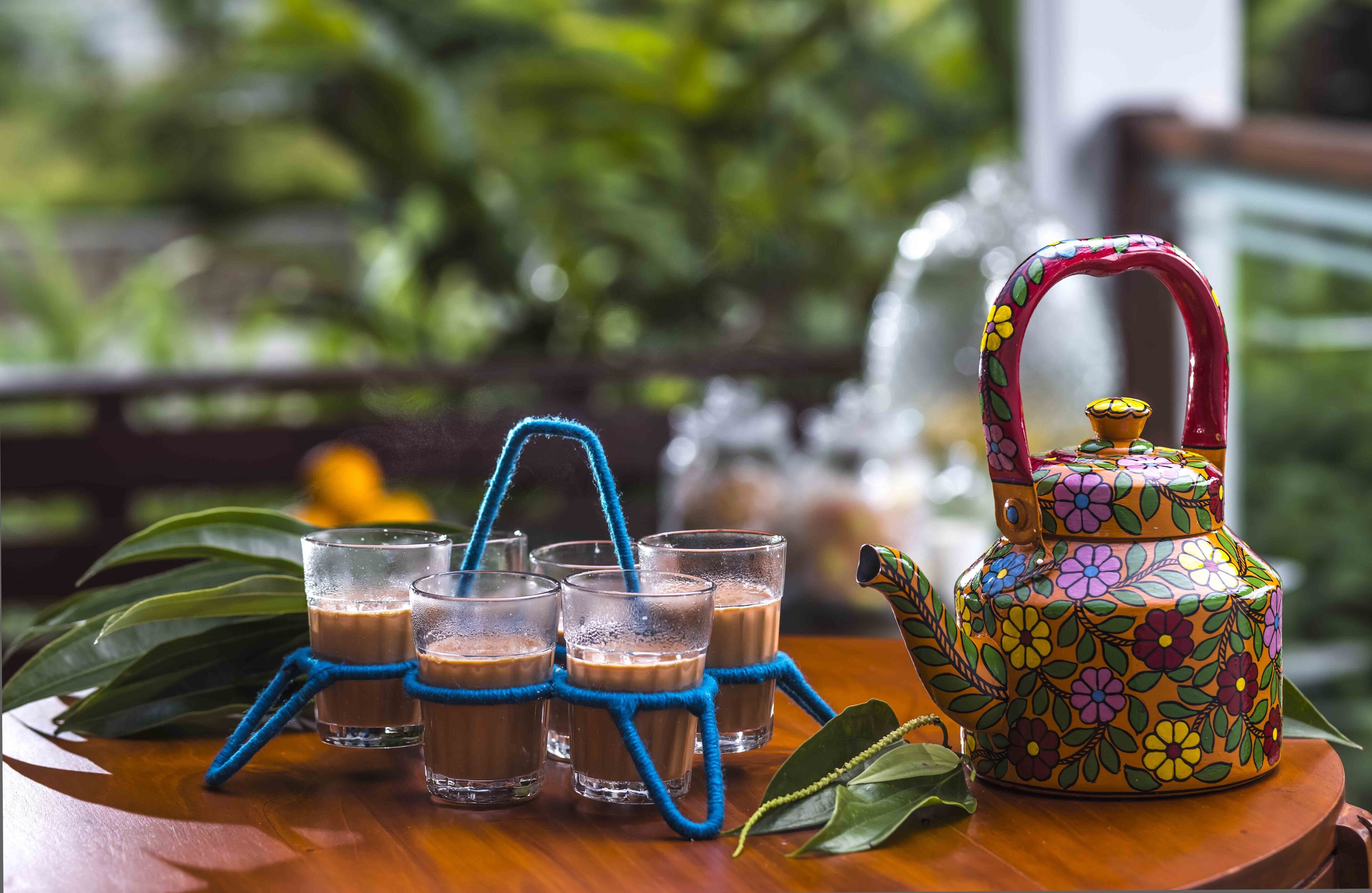 A table with four glasses of a brown beverage, a colorful teapot, and a blue rope.