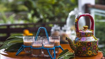 A table with four glasses of a brown beverage, a colorful teapot, and a blue rope.