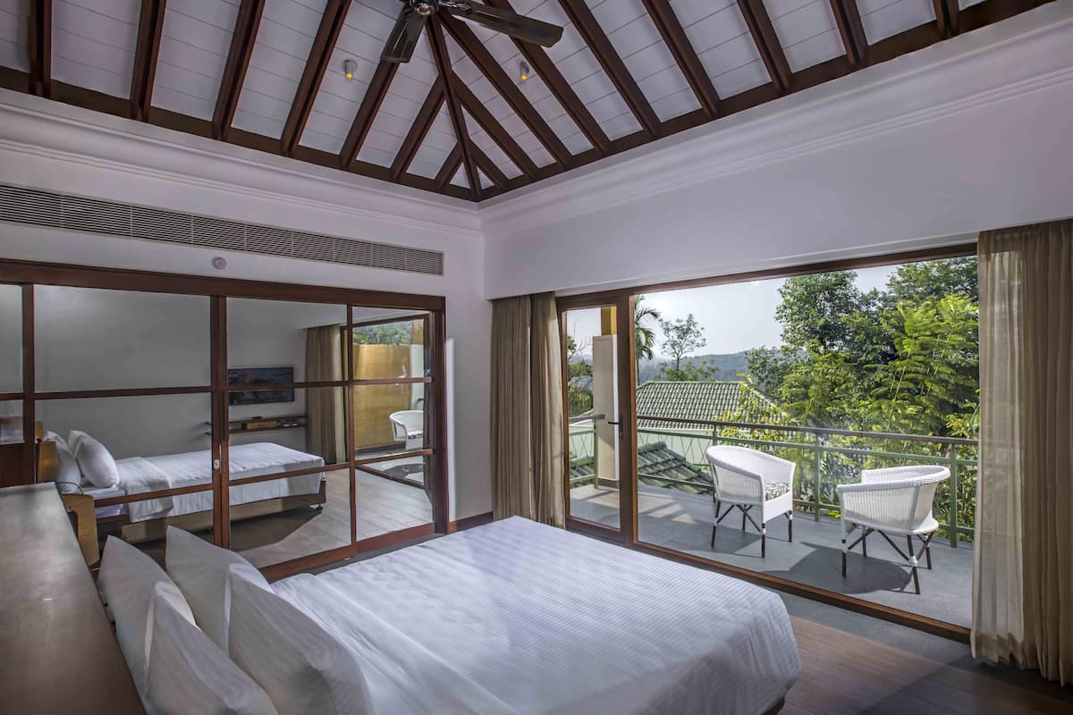Une chambre avec un grand lit, un ventilateur de plafond et un balcon agrémenté de chaises en osier blanches.