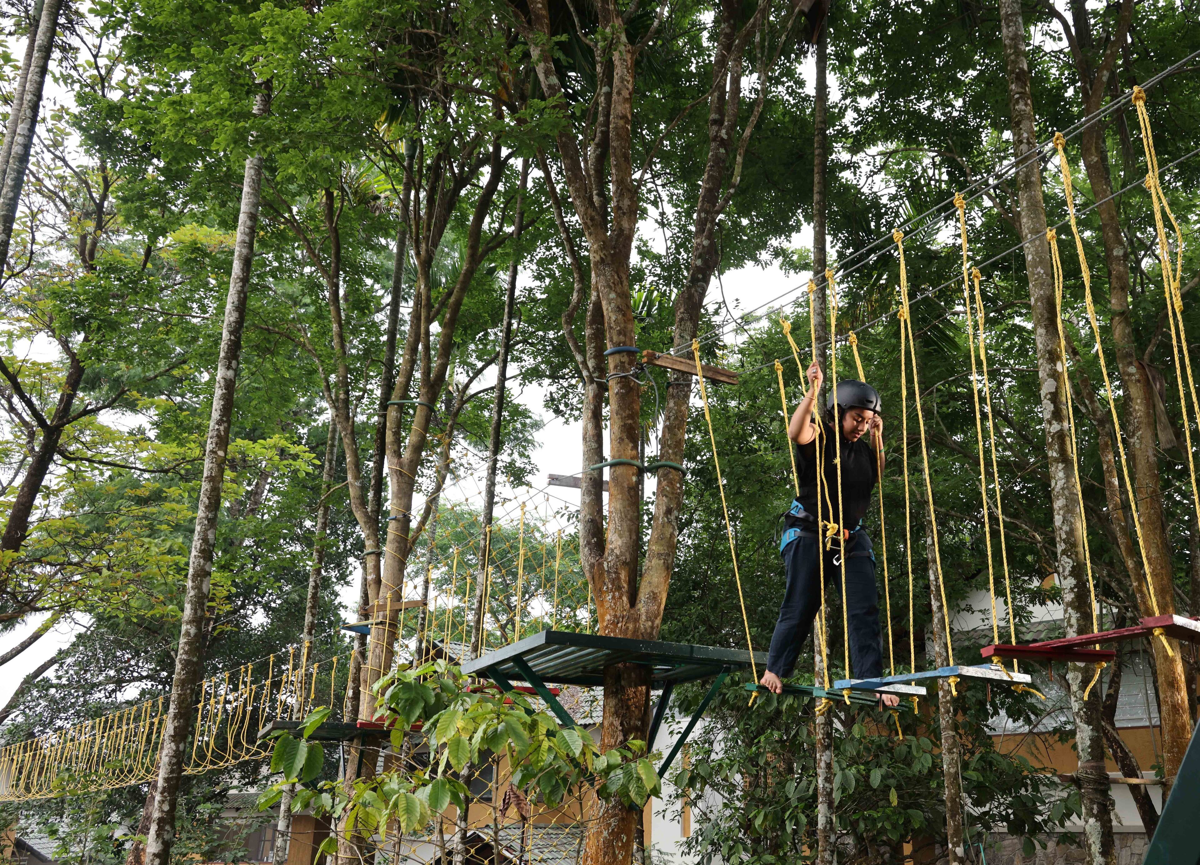 A person navigating a rope course in a forested area with trees and wooden platforms.
