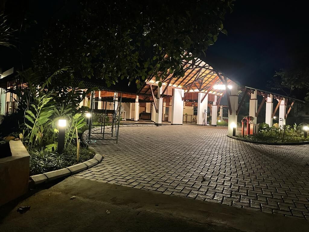 A paved entrance area with a covered structure, surrounded by greenery and illuminated by ambient lighting.