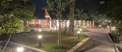 A paved pathway leading to a building with a red roof, surrounded by trees and illuminated by street lamps.