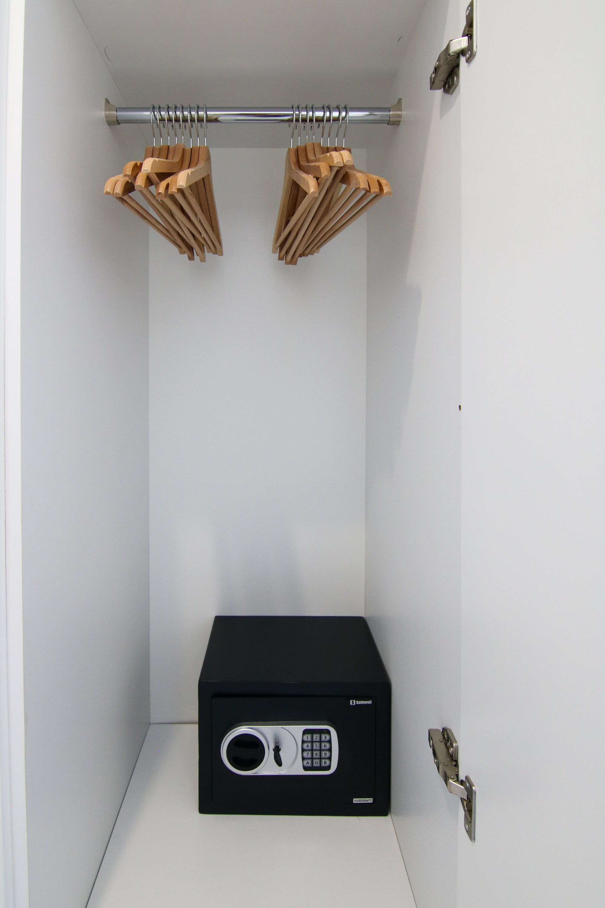 A walk-in closet with a black safe, wooden hangers, and a metal curtain rod.