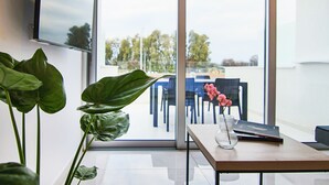 A modern office space with a large window, a desk with a vase of pink flowers, and a plant. - Phaedrus Living: Seaside Luxury Flat Harbour 105 (Paphos)